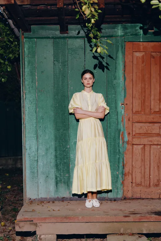 Woman portrait standing in yellow dress at rustic wooden house door, countryside fashion with authenticity and inclusivity