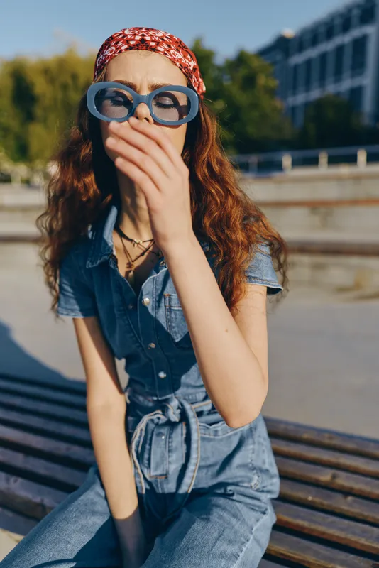 lifestyle woman in modern boho-western denim street style wearing oversized blue sunglasses and red bandana in bright film color outdoor setting