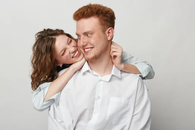 Happy young couple with red hair and curly hair smiling and embracing each other on a light background. Concept of love, affection, and joyful relationship moments.