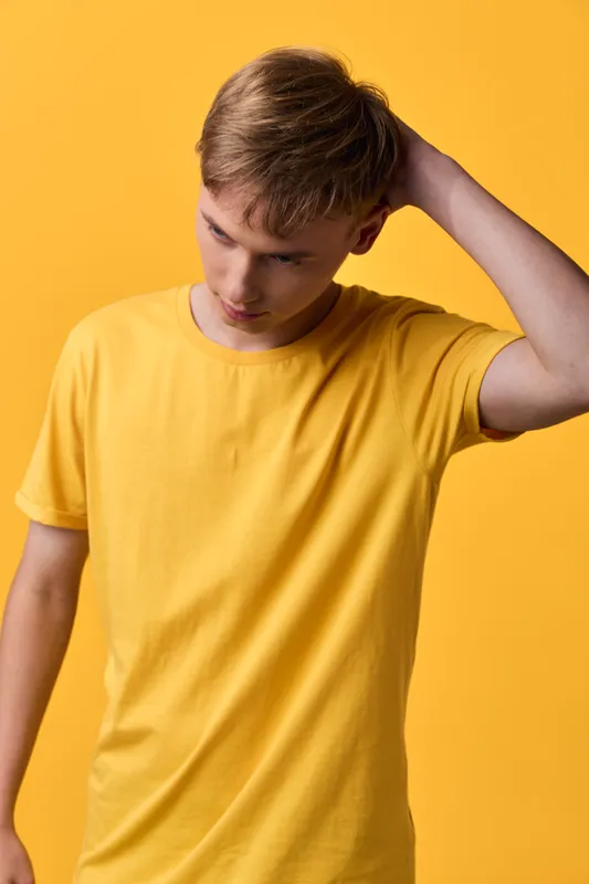 Man in a yellow shirt stands against a yellow background, head tilted, thoughtful expression, casual pose, studio lighting showcasing color harmony and mood for creative stock imagery