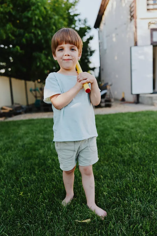 Playful boy holding a toy bat, enjoying a sunny day in the garden. The cheerful atmosphere is perfect for family activities and outdoor fun.