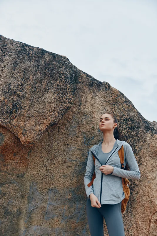 Young woman in athletic clothing standing confidently against a rocky background, representing outdoor adventure and fitness Key attributes include determination and strength