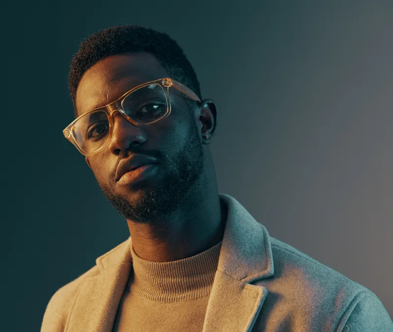 Confident African male model in stylish glasses showcasing a modern, sophisticated look against a gradient background emphasizing contemporary fashion