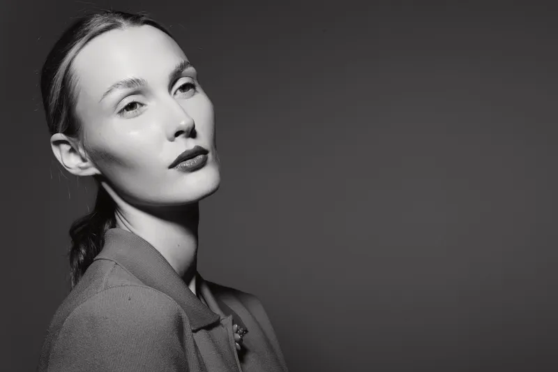 Portrait of a young Caucasian woman with pale skin wearing a textured jacket looking confidently at camera in studio.