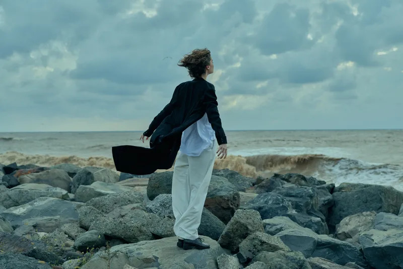 Business traveler walking on rocky shoreline with a briefcase, windy day, ocean horizon, casual formal attire, exploration and movement for travel or career imagery