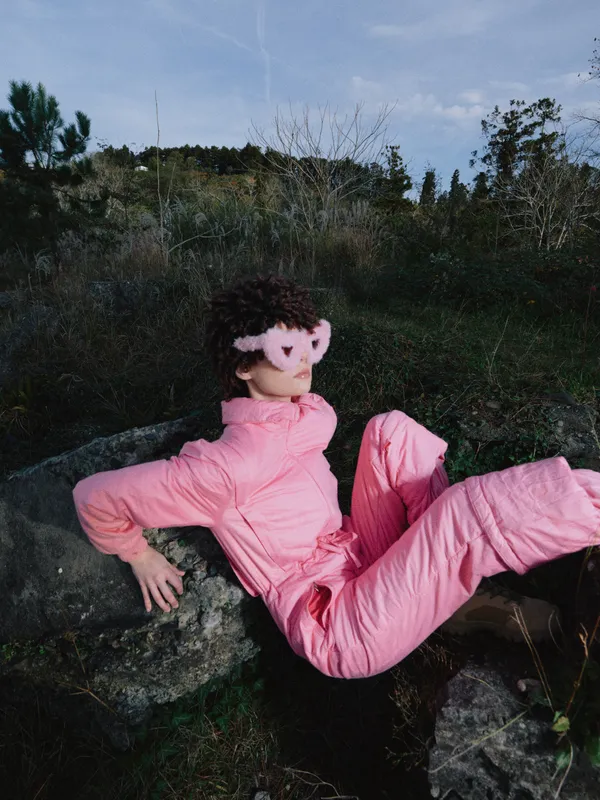 Pink outfit, outdoor pose, natural setting and rock backdrop with a relaxed posture on a mossy rock in nature, portraying casual fashion and serene mood