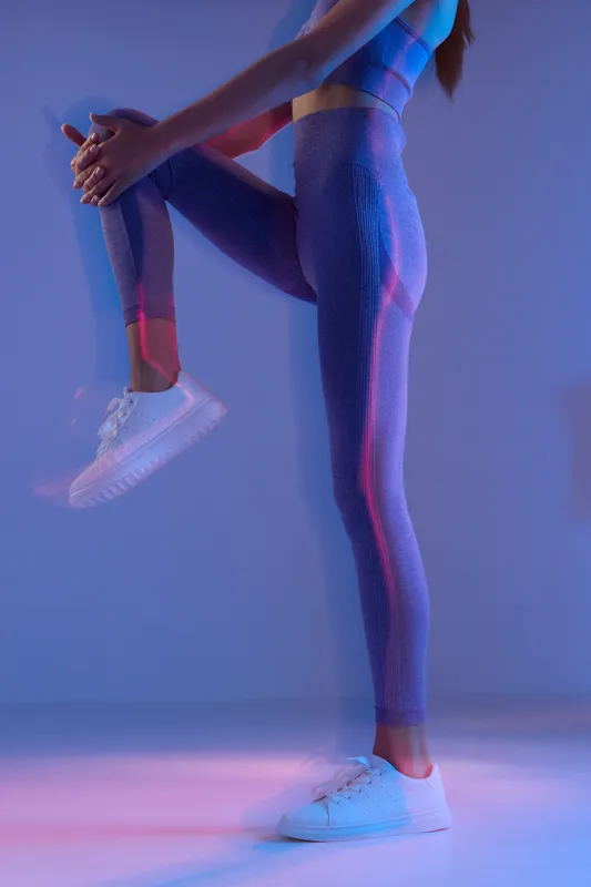 woman sport fitness stretching leg in colorful activewear under soft lighting, preparing for workout with focused posture and white sneakers.