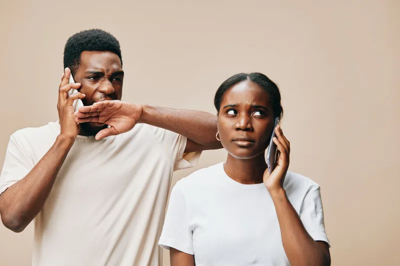 A worried woman looks at her phone while a concerned man talks on his phone, reflecting the tension in communication Stylish, casual outfits in a neutral tone