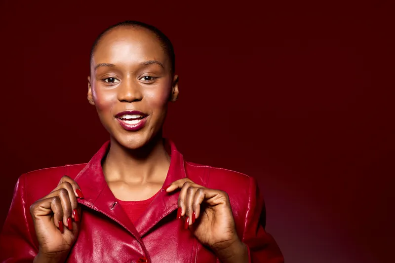 Confident dark skinned African woman wearing a red leather jacket smiles brightly against a red background. Concept of fashion, beauty, style, and empowerment for black women.
