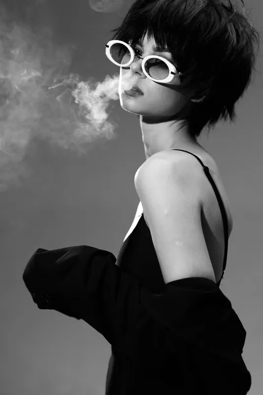 Black and white portrait of a woman with short hair wearing sunglasses and smoking, stylish and mysterious mood.
