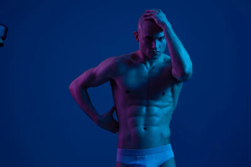 A striking portrait of a man with an athletic physique, showcasing bold blue and pink lighting. The image captures dynamic emotions and intense expression.