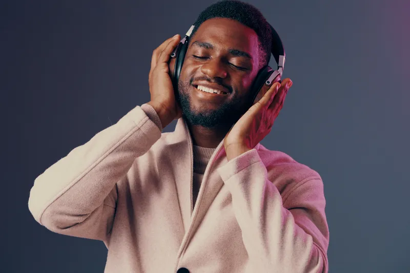 Happy man enjoying music with headphones, dressed in a stylish coat against a gradient background, conveying relaxation and joy through modern lifestyle aesthetics