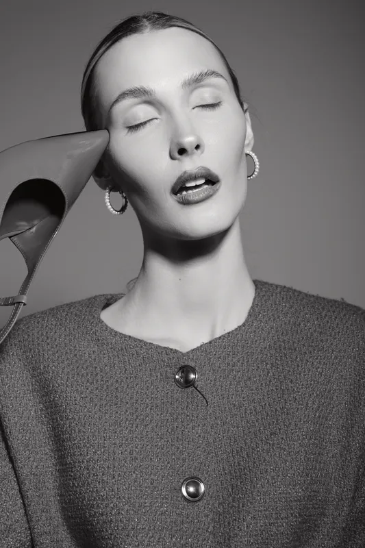 Portrait of a pale white woman with closed eyes and short hair holding a shoe near her head. Fashion concept with minimalistic style and monochrome background.