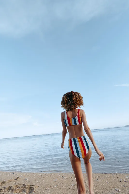 Woman, beach, sea, swimsuit, summer, vacation, walking, rearview, sunlight, striped swimwear, relaxed stance, slim body, looking toward horizon, calm ocean waves, clear sky