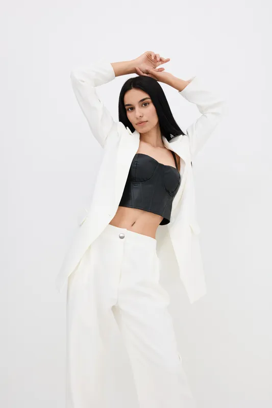young woman posing confidently in white suit and black bustier against plain white background, stylish, modern, fashion, minimalistic studio setting
