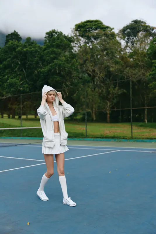 Young athlete in stylish sportswear walking on a tennis court, showcasing confidence and determination amidst a lush green background