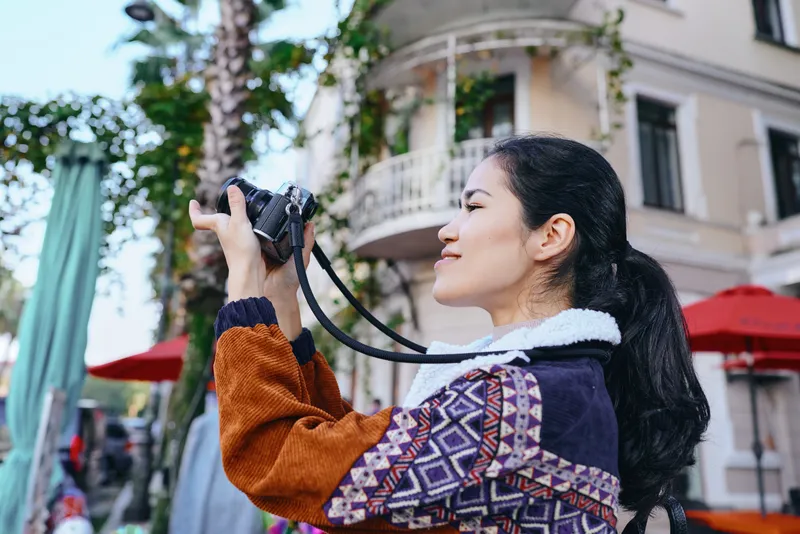 camera photography woman street city outdoors urban scenery lifestyle travel shot capturing a woman with a patterned jacket filming a busy city street cafe scene