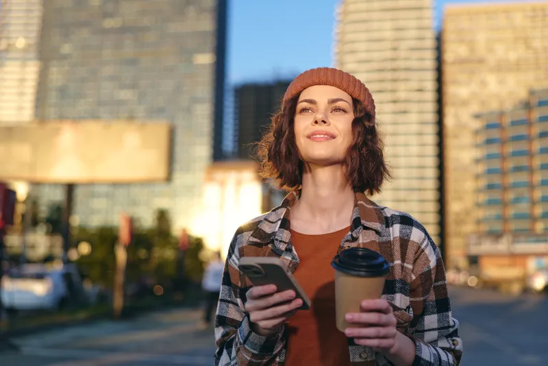 woman holding coffee and smartphone in urban morning, golden glow and candid authenticity capture mindful mood and emotional storytelling of relaxed city lifestyle.