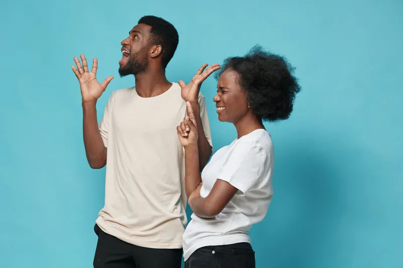 Joyful African American couple celebrating with playful gestures on a bright blue background, expressing happiness together