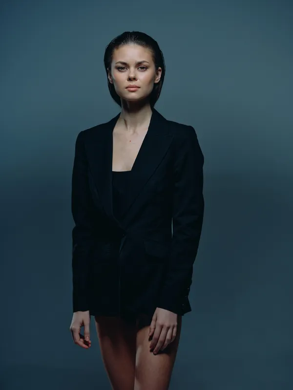 serious woman in black blazer with confident pose and minimal makeup on dark background