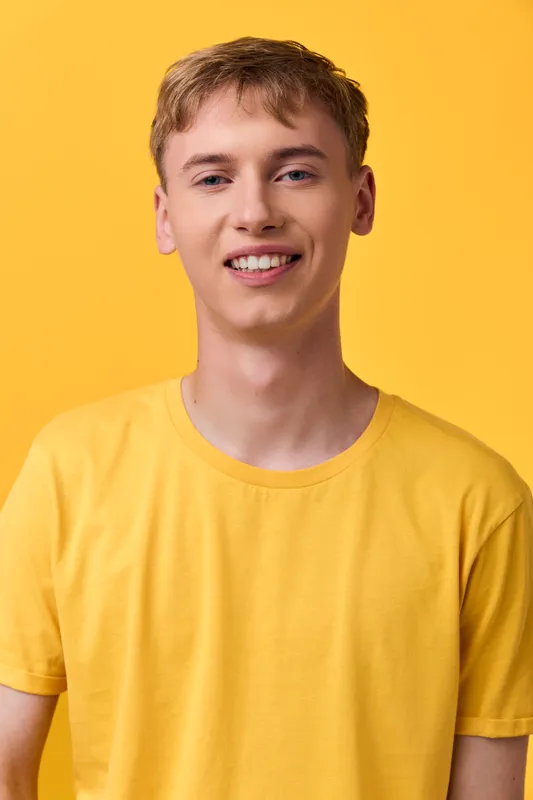 Young man in a yellow T shirt standing against a yellow backdrop, casual fashion, warm smile, bright studio shot, vibrant color harmony for lifestyle branding and approachable vibe for marketing