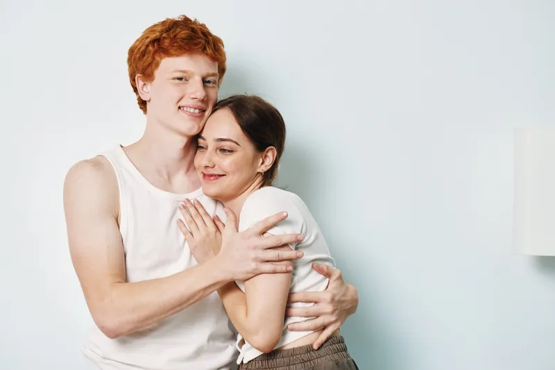Couple hugging and smiling indoors with affection and comfort. Young man and woman embracing gently for love, trust and relationship in casual clothing at home.