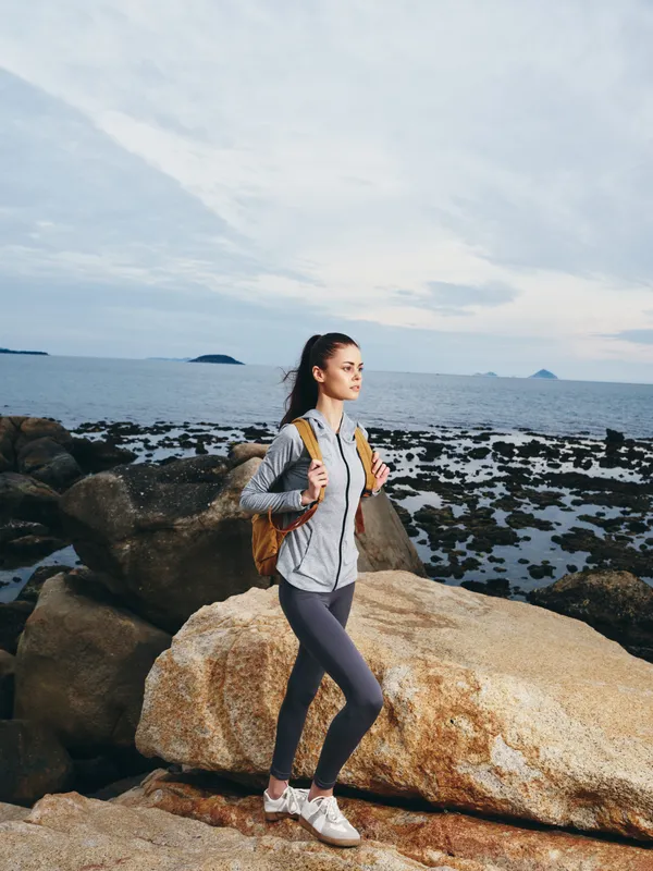 Young athletic woman with a backpack standing on rocky beach, showcasing confidence and adventure, a perfect representation of active lifestyle and nature exploration