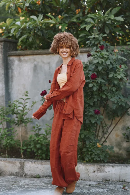 Cheerful woman outdoors wearing rust suit, relaxed pose, sunlight glow, natural colors, garden backdrop, candid lifestyle moment, warm tones, confident smile and glow