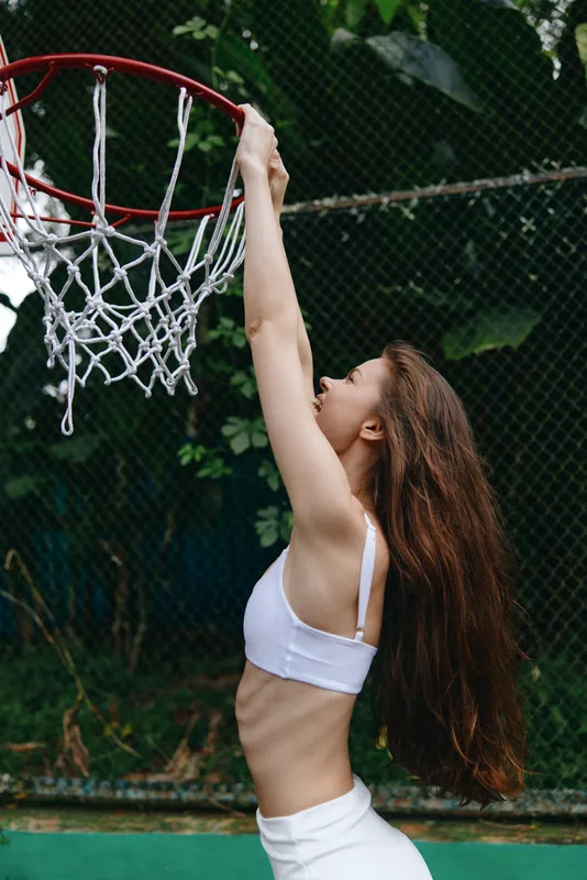 Fit young woman celebrating a basketball win in a sporty outfit, showcasing emotion and strength against a vibrant green background