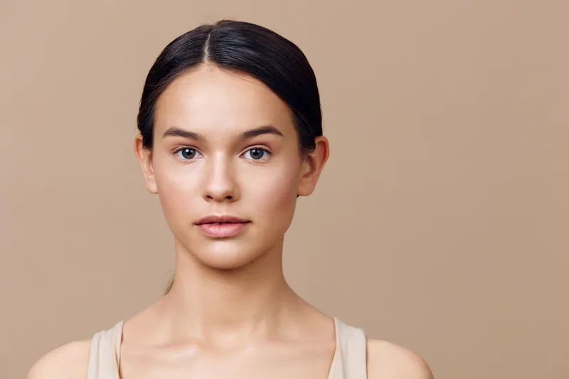 Natural portrait of a young woman with minimal makeup against a soft beige background, conveying serenity and confidence, ideal for beauty and wellness themes