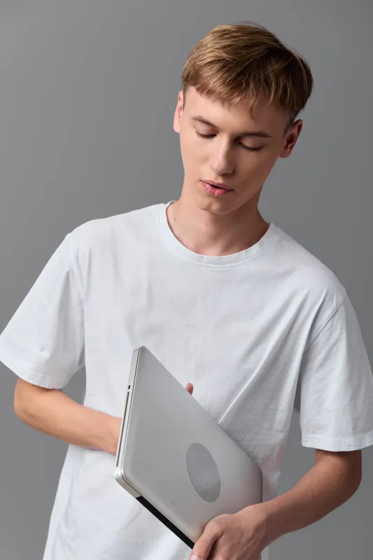 Casual tech scene shows a laptop held by a youth man in a white shirt, focused on screen, ready for study, learning and work, a clean studio setting highlighting digital productivity and education