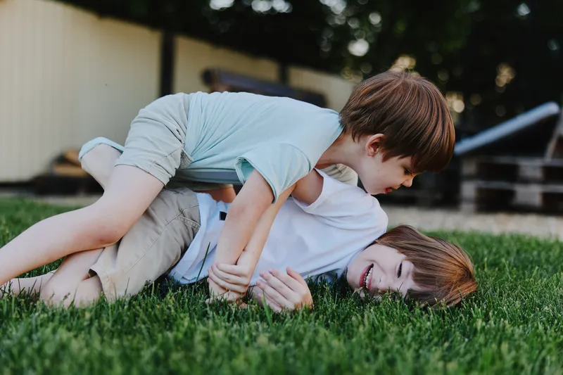 Two young boys playing joyfully in the grass, showcasing their energy and happiness in a sunny outdoor setting, perfect for family-themed content.