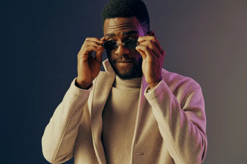 Stylish African American man wearing sunglasses and a light sweater, posing confidently against a gradient background Perfect for fashion and lifestyle concepts