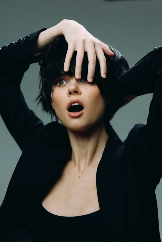 surprised woman with short black hair covering face with hand, expressive emotion, modern style, studio background