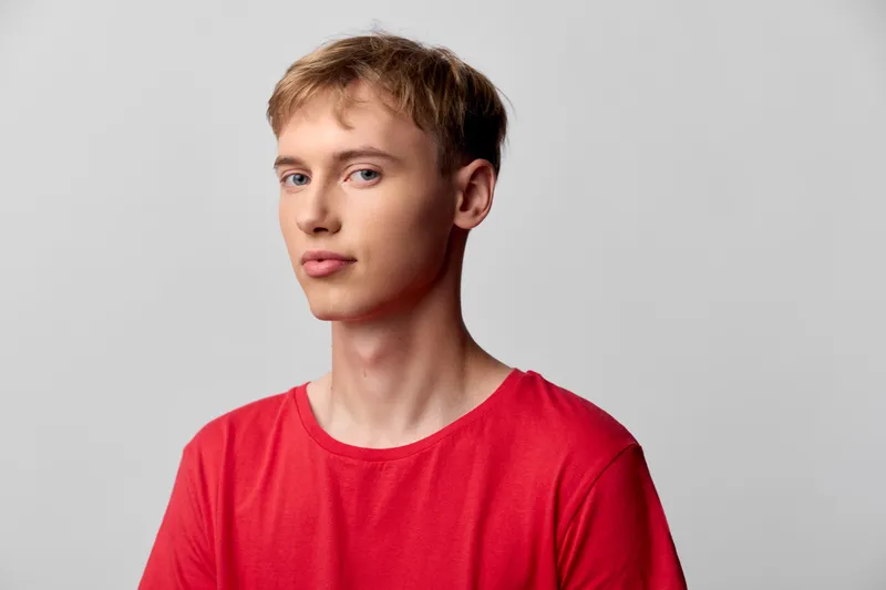 Young man wearing a red shirt posing in a clean studio, casual fashion, neutral background, thoughtful expression, minimal lighting and composition for stock use and lifestyle projects