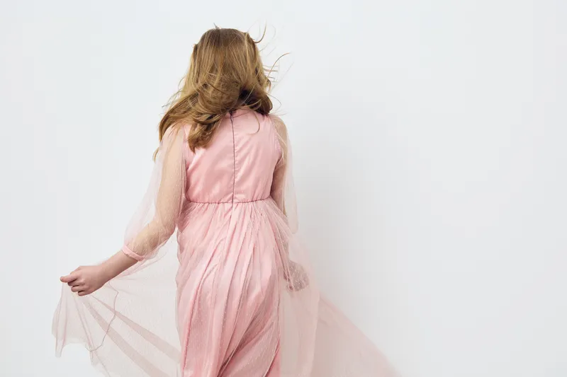 Elegant young woman in a flowing pink dress capturing the essence of spring with her back turned against a soft white background, radiating grace and joy