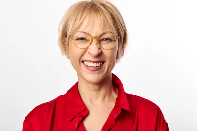 Smiling senior woman with short blond hair and glasses in a red shirt, close up portrait on a white studio background, friendly mood, soft lighting