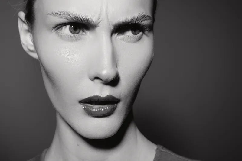 Close-up of a young Caucasian woman with pale skin showing a serious frowning expression. High contrast black and white portrait with dramatic lighting.