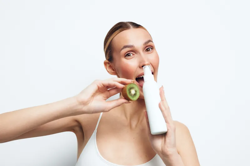 Young woman holding a nasal spray and a sliced kiwi fruit. White background with bright lighting. Concept of health care, natural remedies, and wellness.