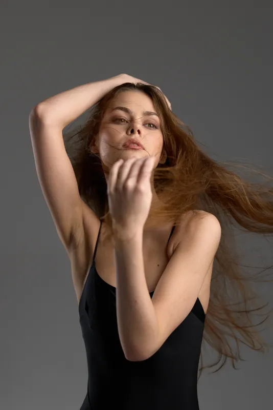 Young woman with flowing red hair in black dress posing gracefully against gray background