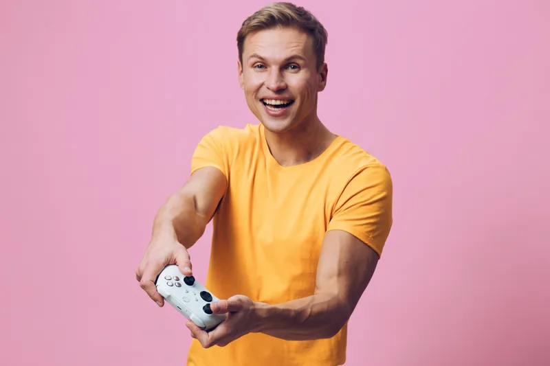 excited young man playing with gamepad hold controller wear yellow t-shirt isolated on pink background digital detox concept with entertainment and leisure