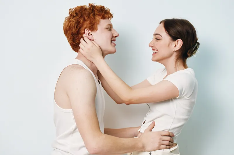 Couple, young man and woman hugging and smiling with white shirts, expressing love, affection and happiness on white background for relationships and connection.