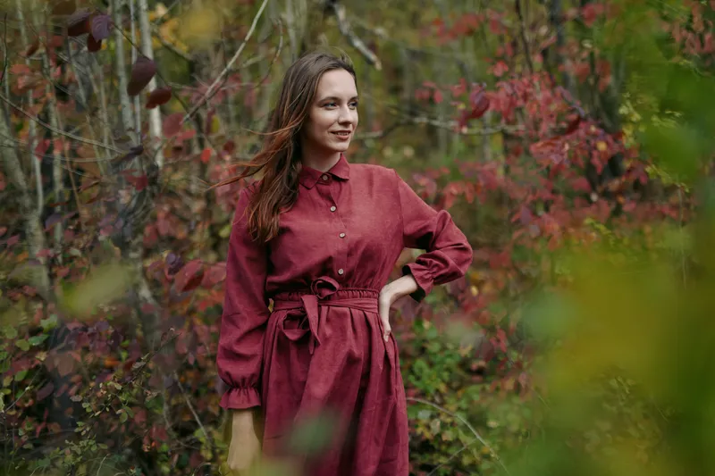 A candid portrait of a young woman in a simple red dress standing among autumn shrubs, conveying natural expression and genuine emotion with authenticity and careful visual accuracy.