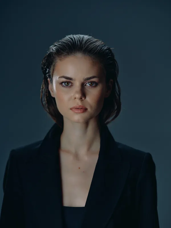 serious woman in black jacket with natural makeup and wet hair against dark background
