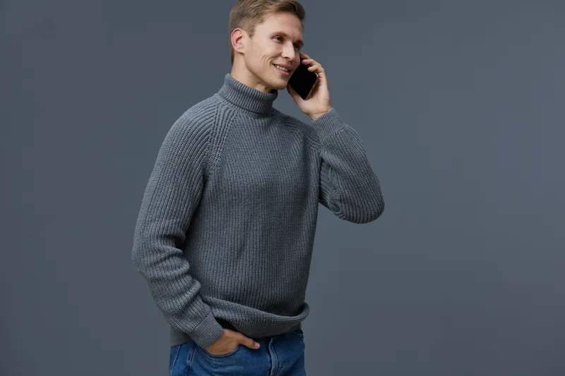 smiling man wearing gray knitted sweater talking phone isolated dark gray background communication digital nomad concept