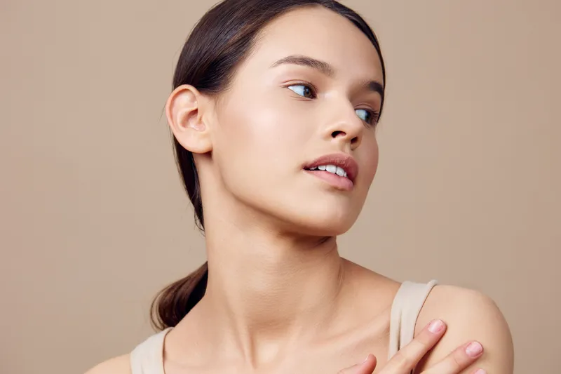 A serene portrait of a young woman with a natural look, showcasing delicate features and soft lighting against a neutral background, representing beauty and self care