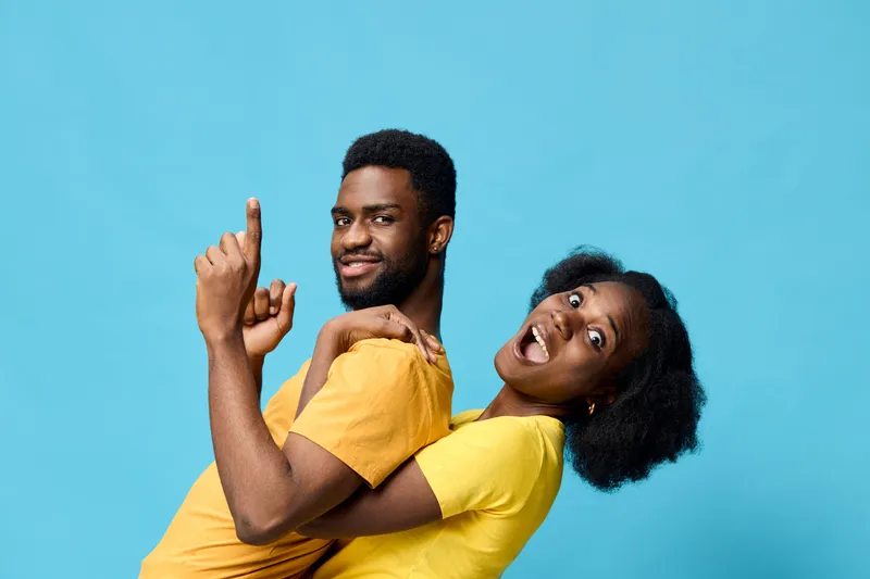 Happy multi ethnic couple enjoying playful moments together against a bright blue background wearing casual yellow shirts, expressing joy and love