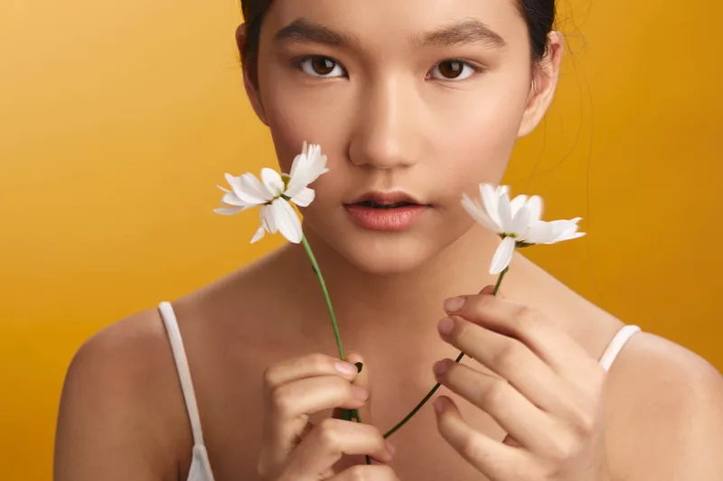 asian woman holds delicate flowers against a warm backdrop, creating a soft, graceful portrait that conveys calm, gentle mood and natural beauty with minimal styling.