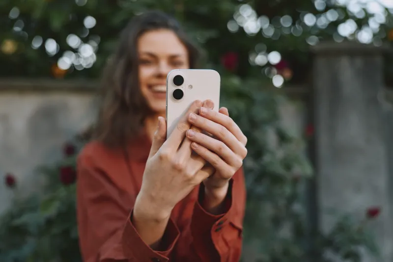 Smiling woman taking a selfie outdoors with a smartphone. Close-up on a natural garden background. Lifestyle concept emphasizing self expression, wellness, and casual everyday moments