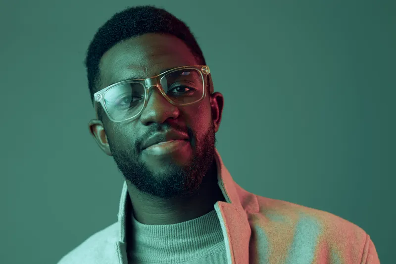Portrait of a confident African man wearing glasses and a stylish sweater, showcasing a warm smile against a soft green backdrop